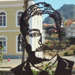 Metalowa rzeźba przedstawiająca twarz ustawiona na tle zabudowy i gór w Ponta do Sol