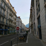 Ulica w centrum Grenoble z zabytkowymi kamienicami, rowerami i górami w tle