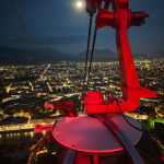 Widok z kabiny kolejki linowej na nocne Grenoble z księżycem nad miastem