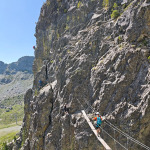 Drewniany most zawieszony na skalnej ścianie Via Ferrata des Lacs Robert w Chamrousse