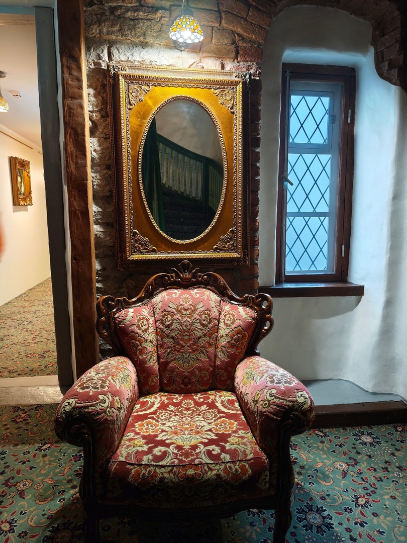 Stylowy fotel, ozdobne lustro i kamienne mury we wnętrzu hotelu St. Olav w Tallinnie